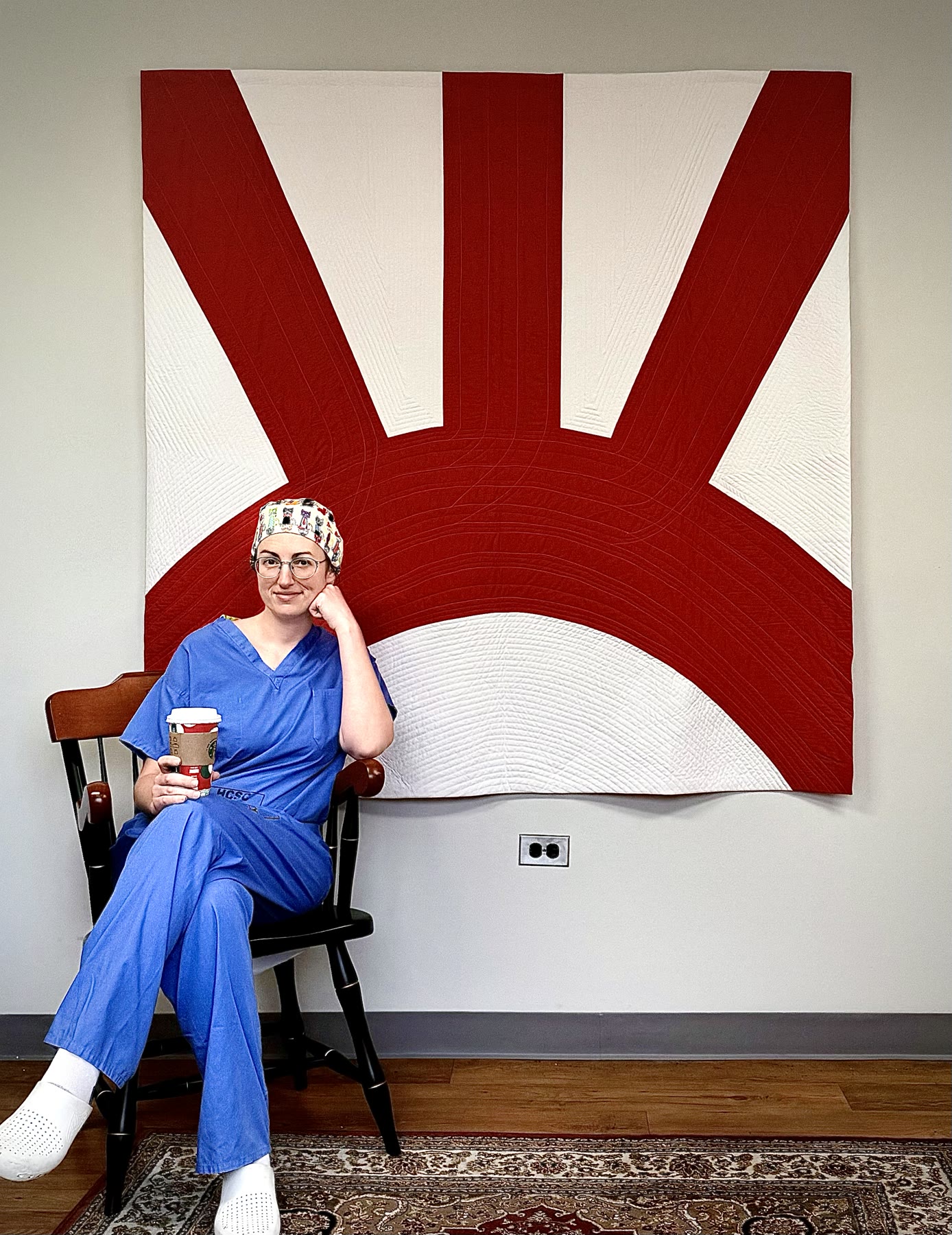 Marissa Famularo seated in scrubs in front of a red and white quilt